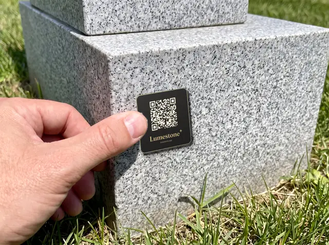 A thumb pressing the plaque onto a granite headstone